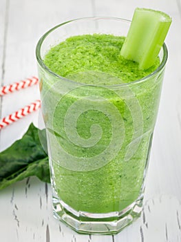 Green smoothie with celery, cucumber, spinach, apple and lemon on a white wooden table