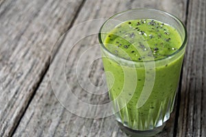 Green Smoothie drink in clear glass, topped with chia seeds, on wood plank