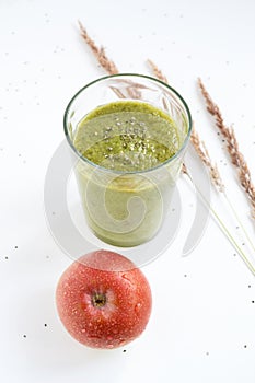 Green smoothie in a glass, spike, red apple.