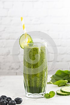 Green smoothie glass with spinach, banana blueberry, cucumber, avocado, bright kitchen background