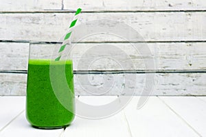 Green smoothie in a glass with straw over white wood