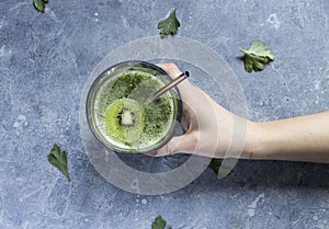 Green smoothie with kiwi slice in glass with metal straw. kiwi, cucumber and parsley green drink on a concrete surface  girl`s han