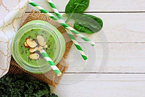 Green smoothie in a mason jar, top view, corner border on white wood