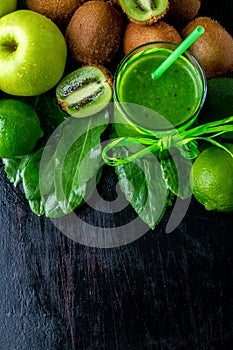 Green smoothie near ingredients for it on black wooden background. Apple, lime, spinach, kiwi. Detox. Healthy drink. Top view. Cop