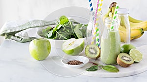 A green smoothie surrounded by fresh raw ingredients used to make it.