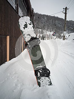 Green snowboard standing in snow with winter mountains in background