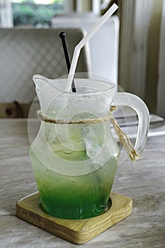 Green soda water with ice in cool jar glass on the coaster square wood put on mable table in restaurant. drinking sweet juice flor