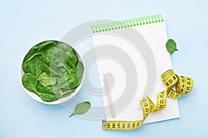 Green spinach leaves, notebook and tape measure on blue table top view. Diet and healthy food concept.