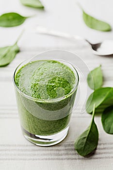 Green spinach smoothie in glass on white table