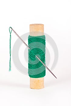 Green spool of thread with a sewing needle on a white background