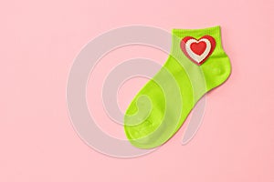 Green sports socks with a red heart on a pink background. Flat lay.