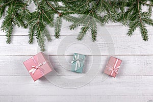 Green spruce branches and pink gift boxes on white wooden background. Christmas concept with copy space