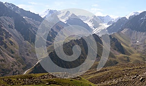 A green spur obscures the river valley among stones and snow-capped peaks in Trans-Ili Alatau