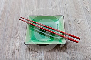 Green square saucer with red chopsticks on gray