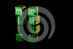 Green Stainless steel cubes simulating ice for cooling drinks on a black surface with a reflection