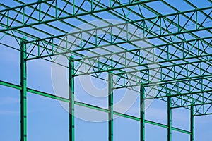 green steel roof of warehouse building structure in construction area against blue sky