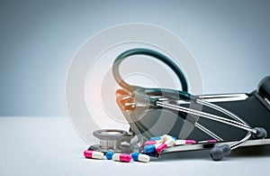 Green stethoscope with pile of antibiotic capsule pills on drug tray and spread on white table. Antimicrobial drug resistance