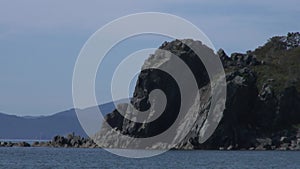 Green stony rocks coastline beach and sea waves water surface in Japan Sea.