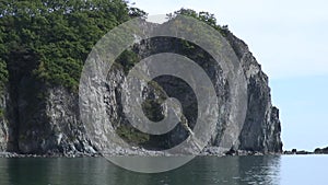 Green stony rocks coastline beach and sea waves water surface in Japan Sea.