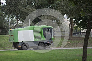 A green Street sweeper vehicle, cleaning the sidewalk