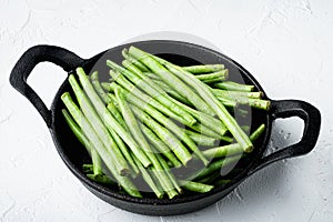 Green string bean, in frying cast iron pan, on white stone  background