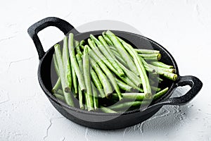 Green string bean, in frying cast iron pan, on white stone  background