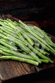 Green string bean, on wooden cutting board, on old dark  wooden table background