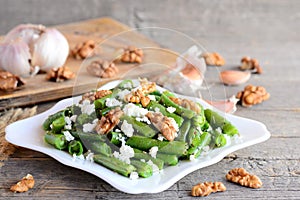 Green string beans salad with cottage cheese and walnuts on a white plate and old wooden table Closeup