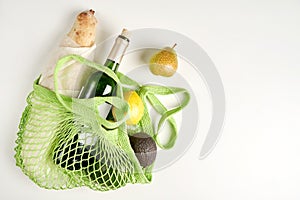 Green string eco shopping bag with vegatables, bread and bottle of vine on grey