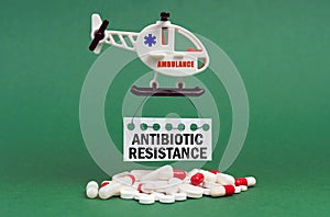 On a green surface, an ambulance helicopter, pills and a white sign with the inscription - ANTIBIOTIC RESISTANCE