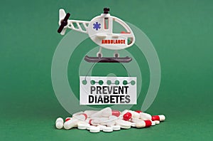 On a green surface, an ambulance helicopter, pills and a white sign with the inscription - PREVENT DIABETES