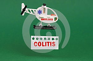 On a green surface, an ambulance helicopter with a sign - COLITIS