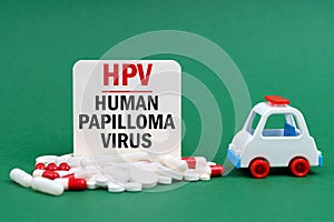 On a green surface, an ambulance, pills and a white sign with the inscription - human papilloma virus