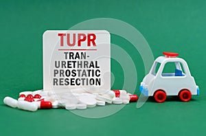 On a green surface, an ambulance, pills and a white sign with the inscription - TransUrethral Prostatic Resection