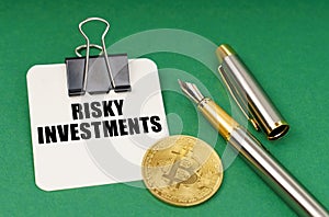 On a green surface, a bitcoin coin, a pen and a sheet of paper with the inscription - risky investments