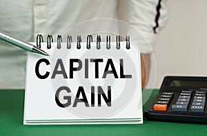 On a green surface, a calculator and a notepad with the inscription - capital gain