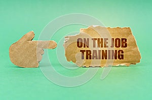 On a green surface, a cardboard hand points to a sign with the inscription - On the Job Training