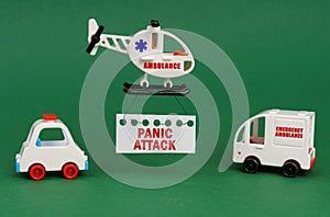 On a green surface, cars and an ambulance helicopter with a sign - PANIC ATTACK