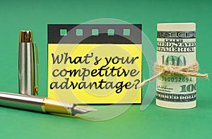 On a green surface, a dollars, a notepad and yellow stickers with the inscription - What is Your Competitive Advantage