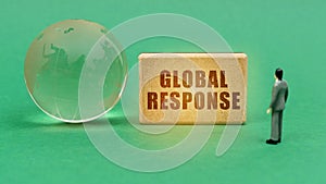 On the green surface is a globe and a figurine of a man who looks at a sign with the inscription - global response