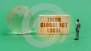 On the green surface is a globe and a figurine of a man who looks at a sign with the inscription -Think global act local