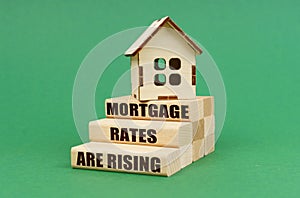 On a green surface, the house stands on blocks. Blocks with the inscription - Mortgage rates are rising