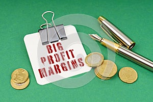 On a green surface, a pen, coins and a notepad with the inscription - Big Profit Margins