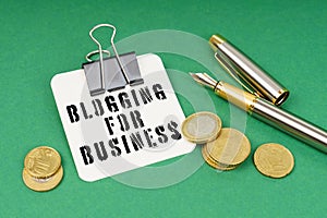 On a green surface, a pen, coins and a notepad with the inscription - Blogging for Business