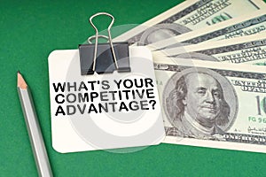 On a green surface, a pen, dollars and paper with the inscription - What is Your Competitive Advantage