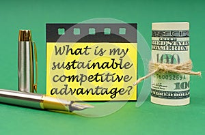 On a green surface, a pen, dollars, a yellow stickers with the inscription What Is My Sustainable Competitive Advantage