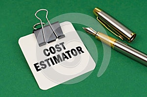 On a green surface, a pen and a sheet of paper with the inscription - Cost estimator