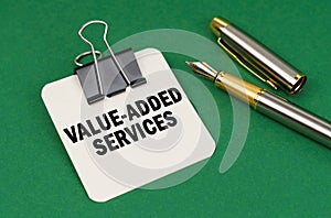 On a green surface, a pen and a sheet of paper with the inscription - Value-Added Services