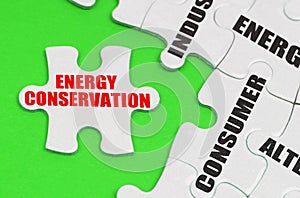 On a green surface are white puzzles with text, on a separate puzzle there is an inscription - Energy Conservation