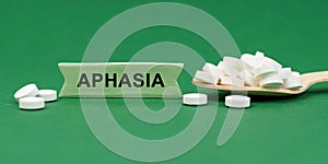 On a green surface, a wooden spoon with pills and a sign with the inscription - Aphasia